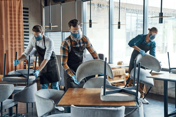 Young male waiters in protective workwear arranging furniture in restaurant Young male waiters in protective workwear arranging furniture in restaurant